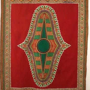 May include: A red fabric with a central green and white geometric design. The design is framed by a border of paisley and geometric patterns in shades of green, orange, and brown. The fabric has a rectangular shape.