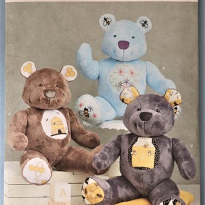 May include: A Simplicity sewing pattern envelope R11696 featuring three plush teddy bears in brown, light blue, and dark gray. Each bear has unique bee and honeycomb fabric accents on the ears, feet, and chest patches. The text includes Simplicity, R11696, U.S. ONE SIZE, and Carla Reiss.