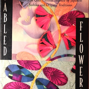 May include: A book cover titled "Fabled Flowers" by Kumiko Sudo. The cover features a colorful floral design with pink, blue, and orange petal shapes. The text reads "Innovative Quilt Patterns Inspired by Japanese Sashiko and Origami Traditions."