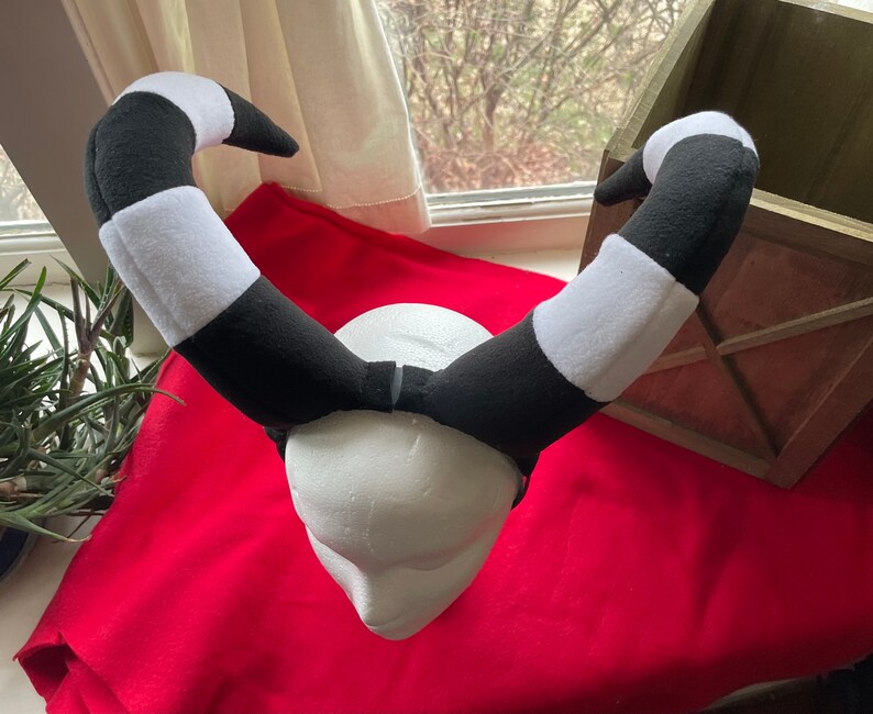 May include: Black and white striped headband with a foam head form. The headband is made of soft, plush fabric.