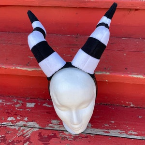 May include: Black and white striped headband with horns. The headband is made of soft, plush fabric and is perfect for a costume or cosplay.