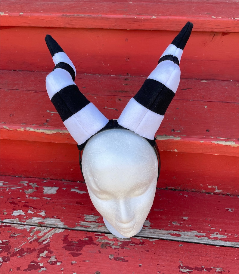 May include: Black and white striped headband with horns. The headband is made of soft, plush fabric and is perfect for a costume or cosplay.