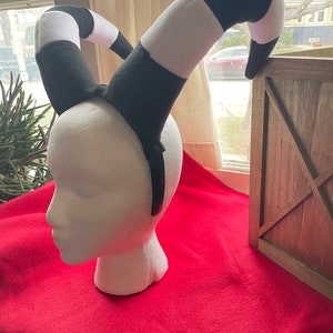 May include: Black and white striped headband with two curled horns. The headband is made of soft fabric and is perfect for a costume or cosplay.