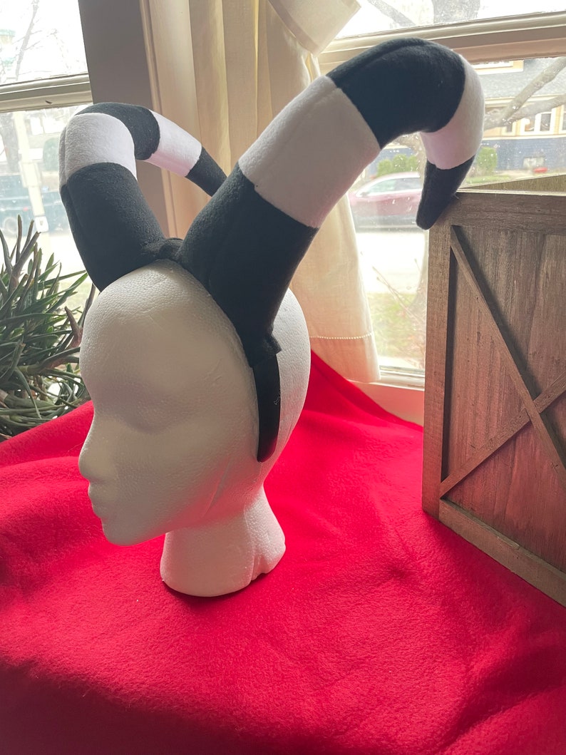 May include: Black and white striped headband with two curled horns. The headband is made of soft fabric and is perfect for a costume or cosplay.