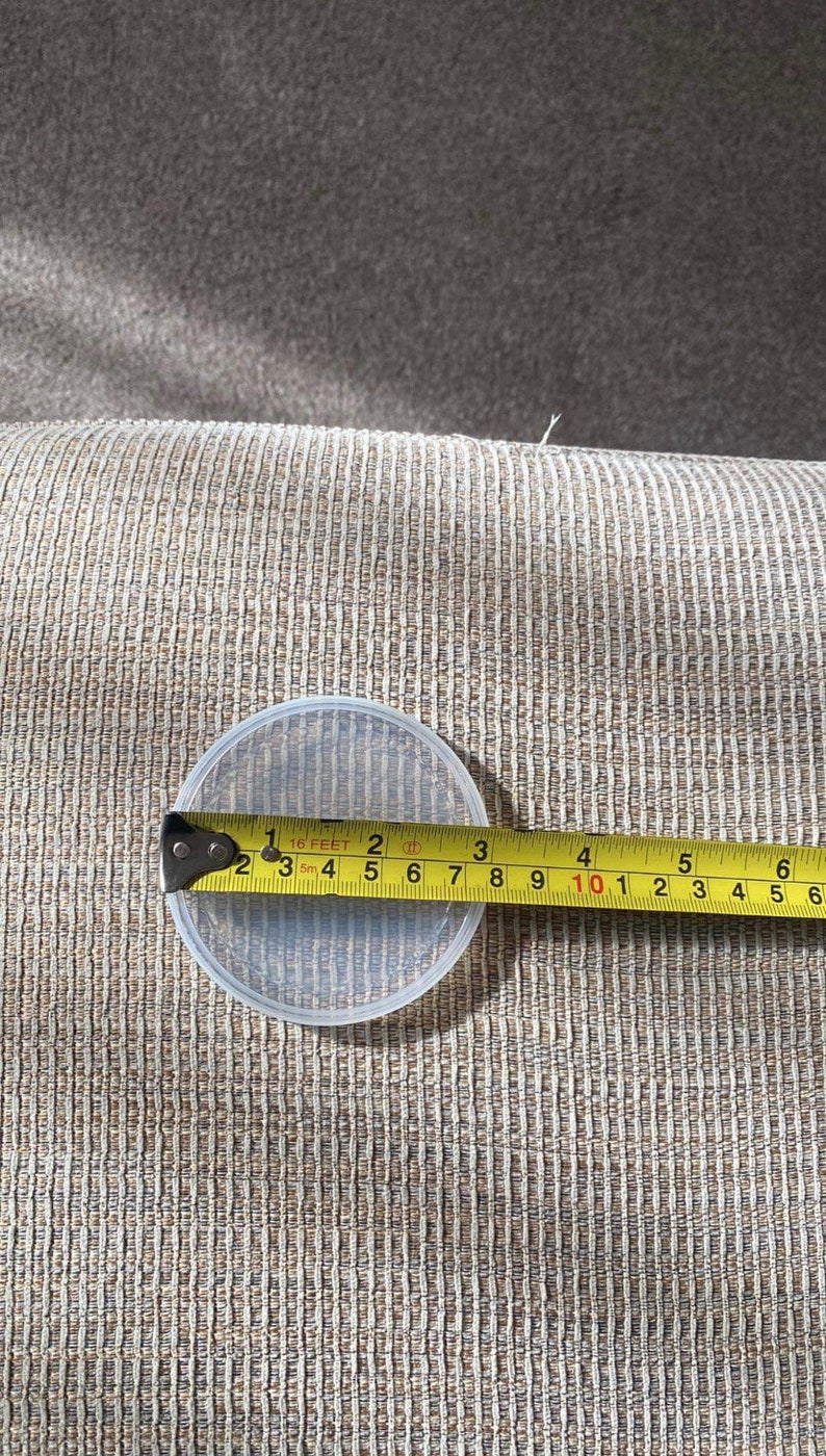 May include: A clear, round plastic container is measured with a tape measure. The container is approximately 4 inches in diameter. The tape measure shows measurements in inches and feet.