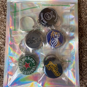Puede incluir: Un paquete transparente e iridiscente que contiene cinco llaveros de tap&oacute;n de botella. Los llaveros presentan logotipos de Jack Daniel's, Coors, Heineken y Camaro. Los llaveros est&aacute;n en fundas de pl&aacute;stico individuales.