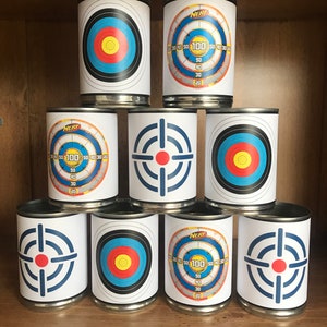 May include: Nine metal cans with different target designs printed on them. The targets are blue, red, yellow, and white. The cans are stacked in a pyramid shape on a wooden shelf. The cans are labeled "NERF" and have numbers on them.