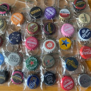 Puede incluir: Colecci&oacute;n de llaveros con chapas de botellas de varias marcas, como Heineken, Corona y Jack Daniel's. Cada chapa est&aacute; en una bolsa de pl&aacute;stico transparente con un llavero de metal. Las chapas muestran logotipos y texto coloridos.