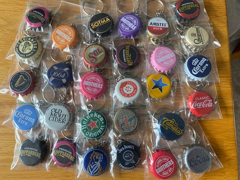 Puede incluir: Colecci&oacute;n de llaveros con chapas de botellas de varias marcas, como Heineken, Corona y Jack Daniel's. Cada chapa est&aacute; en una bolsa de pl&aacute;stico transparente con un llavero de metal. Las chapas muestran logotipos y texto coloridos.