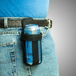 May include: A black leather can holder with a blue and silver energy drink can inside. The holder is attached to a brown leather belt.