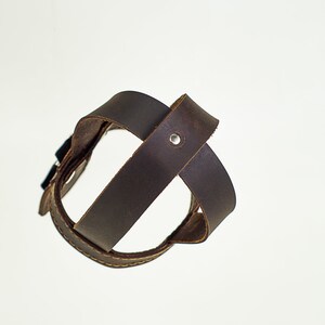 May include: A brown leather bottle holder with a metal rivet. The holder is designed to hold a bottle of wine or other beverage.