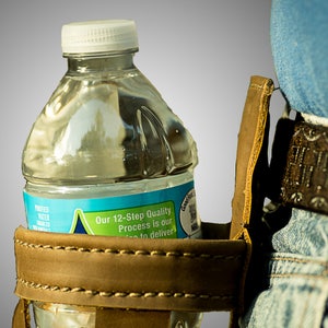 May include: A brown leather water bottle holder with a stitched seam. A clear plastic water bottle with a blue label is in the holder. The label reads "Our 12-Step Quality Process is our way to deliver."
