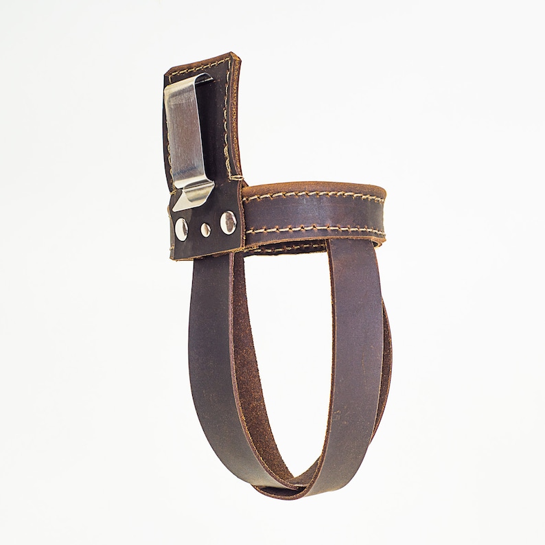 May include: A brown leather bottle holder with a metal clip. The holder has a stitched design and is made of thick leather.