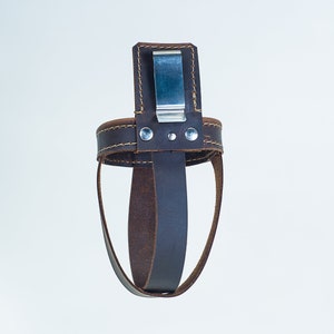 May include: A brown leather bottle holder with a metal clip. The holder is designed to fit around a bottle and has a strap that can be used to secure it to a belt.