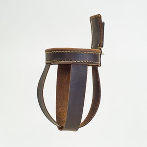 May include: A brown leather bottle holder with a stitched top and a strap. The holder is designed to hold a bottle upright.