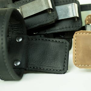 May include: Close-up of a black leather wallet with a metal money clip. The wallet has a stitched edge and two metal rivets.