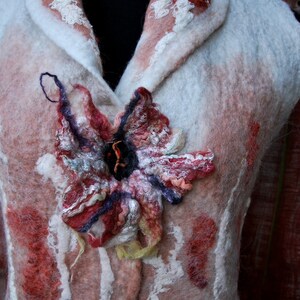 May include: A white felted vest with a red and white collar and a large, colorful flower design on the front.