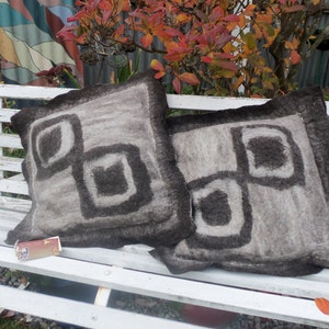 May include: Two grey and black patterned throw pillows with a geometric design on a white wooden bench.
