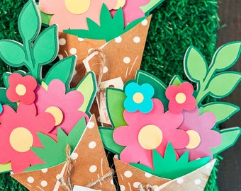 May include: Paper flower bouquets with pink, red, and blue flowers, green leaves, and yellow centers. The bouquets are in brown paper cones with white polka dots, tied with twine, and include tags that say "Happy Mother's Day" and names.