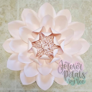 May include: A large, light pink paper flower with multiple layers of petals. The center of the flower has a textured, fringed design. The text "Forever Petals by Vee" is visible in the lower right corner.