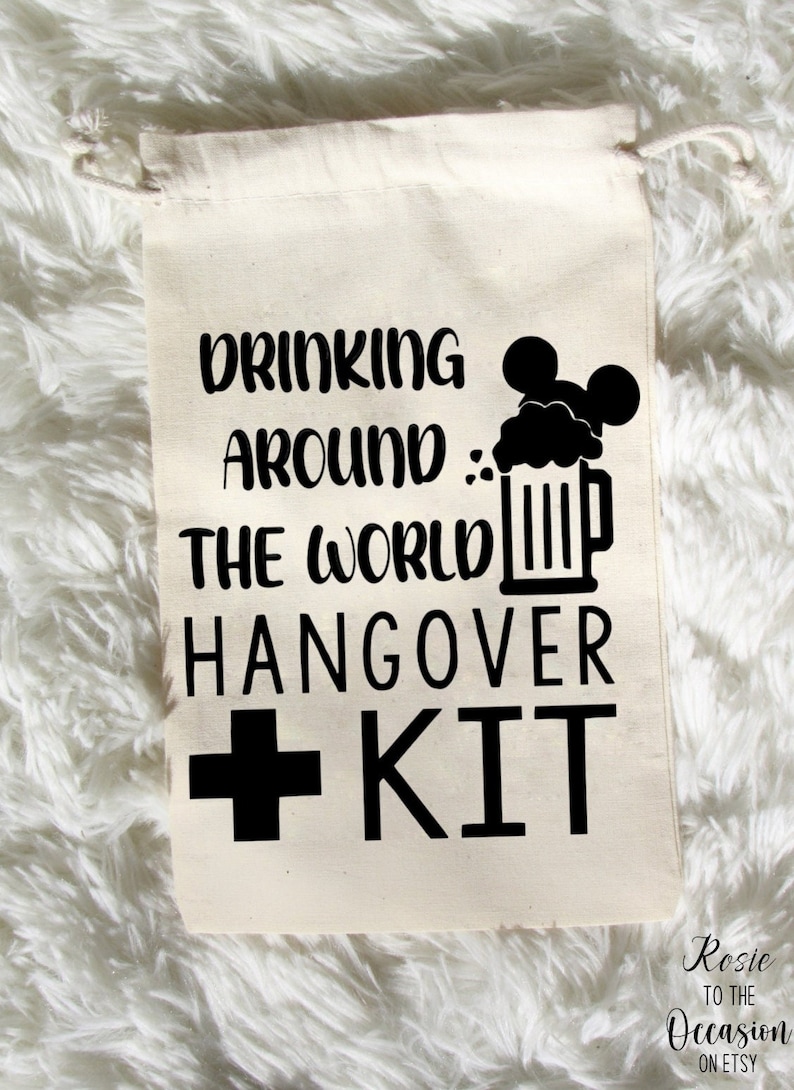 K&ouml;nnte beinhalten: Ein wei&szlig;er Baumwollbeutel mit Kordelzug und schwarzem Text, der "Drinking Around The World Hangover Kit" lautet, mit einem schwarzen Pluszeichen und dem Wort "KIT" in gro&szlig;en Buchstaben. Neben dem Text befindet sich eine schwarze Silhouette eines Bierkruges mit einer Mickey-Maus-Kopf oben drauf.