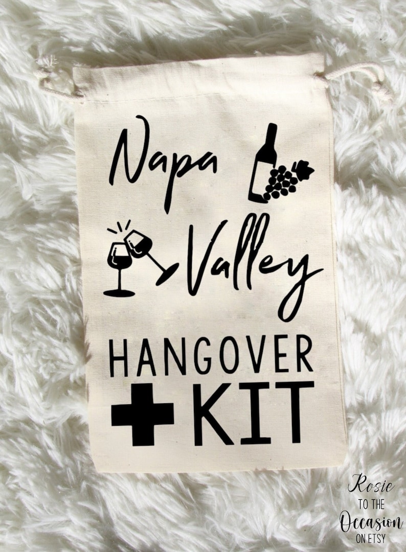 May include: White canvas drawstring bag with black text and graphics that reads "Napa Valley Hangover Kit" with a wine bottle, grapes, and two wine glasses.