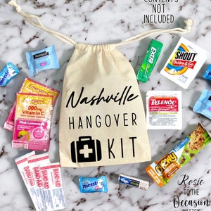 Op de afbeelding: Een witte canvas tas met de tekst "Nashville Hangover Kit" erop gedrukt. De tas is gevuld met verschillende items, waaronder pijnstillers, maagzuurremmers, vitamine C-zakjes, kauwgom en een chocolade reep. De tekst "*CONTENTS NOT INCLUDED" is bovenaan de afbeelding gedrukt.