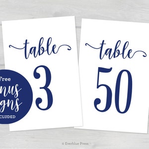 May include: Two white table number signs with navy blue text. The text reads "table" followed by the number "3" on one sign and "50" on the other.