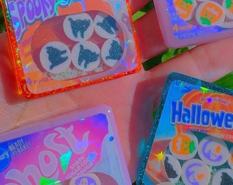 May include: Four miniature square resin charms resembling packages of Ready to Bake cookie dough. The packages feature holographic labels with text including Spooky Cat, Pumpkin, Ghost, and Halloween, each displaying small round cookie dough slices.