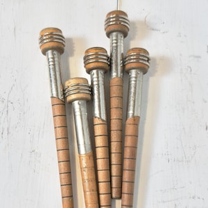 May include: A collection of six vintage wooden spools with metal and wood accents. The spools have a cylindrical shape with a wider top and a narrower base. The wood is light brown with dark lines, and the metal is silver. The spools are arranged on a white surface.