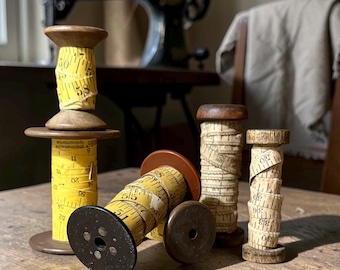 Puede incluir: Una colección de cuatro carretes de madera envueltos en cintas métricas antiguas. Un carrete está erguido, uno está inclinado y dos están en posición vertical. Las cintas son amarillas y blanquecinas con marcas numéricas negras en centímetros.