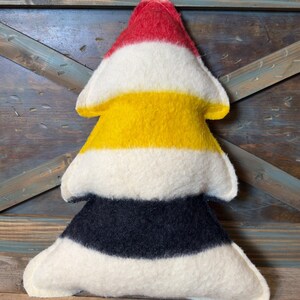Puede incluir: Un coj&iacute;n suave con forma de &aacute;rbol que presenta franjas horizontales de fieltro en colores rojo, blanco, amarillo, blanco, negro y blanco. La decoraci&oacute;n rellena tiene una punta superior y una base ancha de tres niveles con costuras.