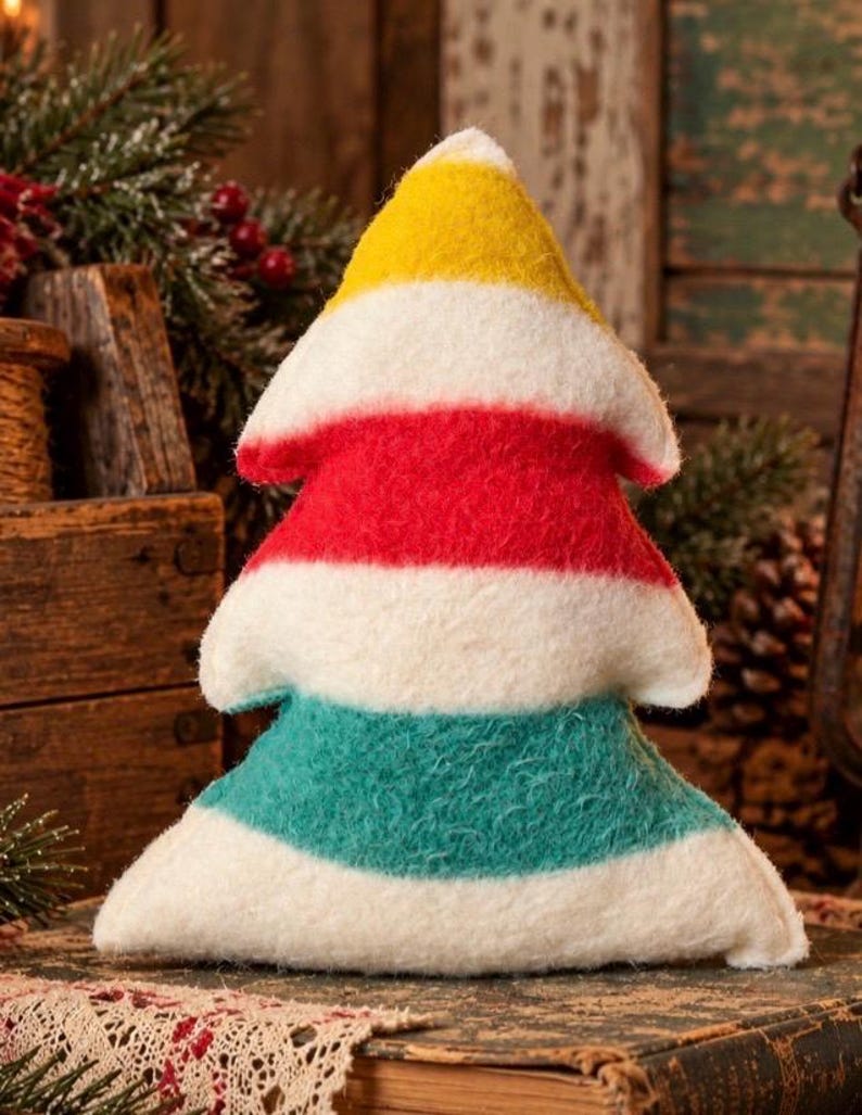 Puede incluir: Un adorno de peluche con forma de &aacute;rbol hecho de material de fieltro difuso. El dise&ntilde;o presenta rayas horizontales en amarillo, blanco, rojo, blanco, verde azulado y blanco, dispuestas desde la punta hasta la base ancha.