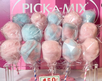 Puede incluir: Exhibición de algodón de azúcar rosa y azul, envuelto individualmente en plástico transparente, sobre soportes transparentes. El fondo presenta el texto "PICK-A-MIX" sobre un fondo a rayas rosas y blancas. Un letrero muestra el precio.