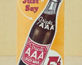 Puede incluir: Anuncio vintage de Triple AAA Root Beer. La imagen presenta una botella de root beer con una etiqueta roja y blanca, sobre un fondo amarillo. El texto incluye "Just Say" y el precio "5¢".
