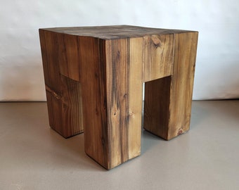 Könnte beinhalten: Ein rustikaler Holzhocker mit quadratischer Oberseite und einem einzigartigen offenen Design an den Seiten. Der Hocker ist aus dunkelbraunem Holz mit sichtbarer Maserung.