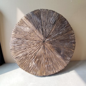 May include: A round wooden wall decor with a radial pattern of wood slats. The wood is a dark brown color with a natural finish.