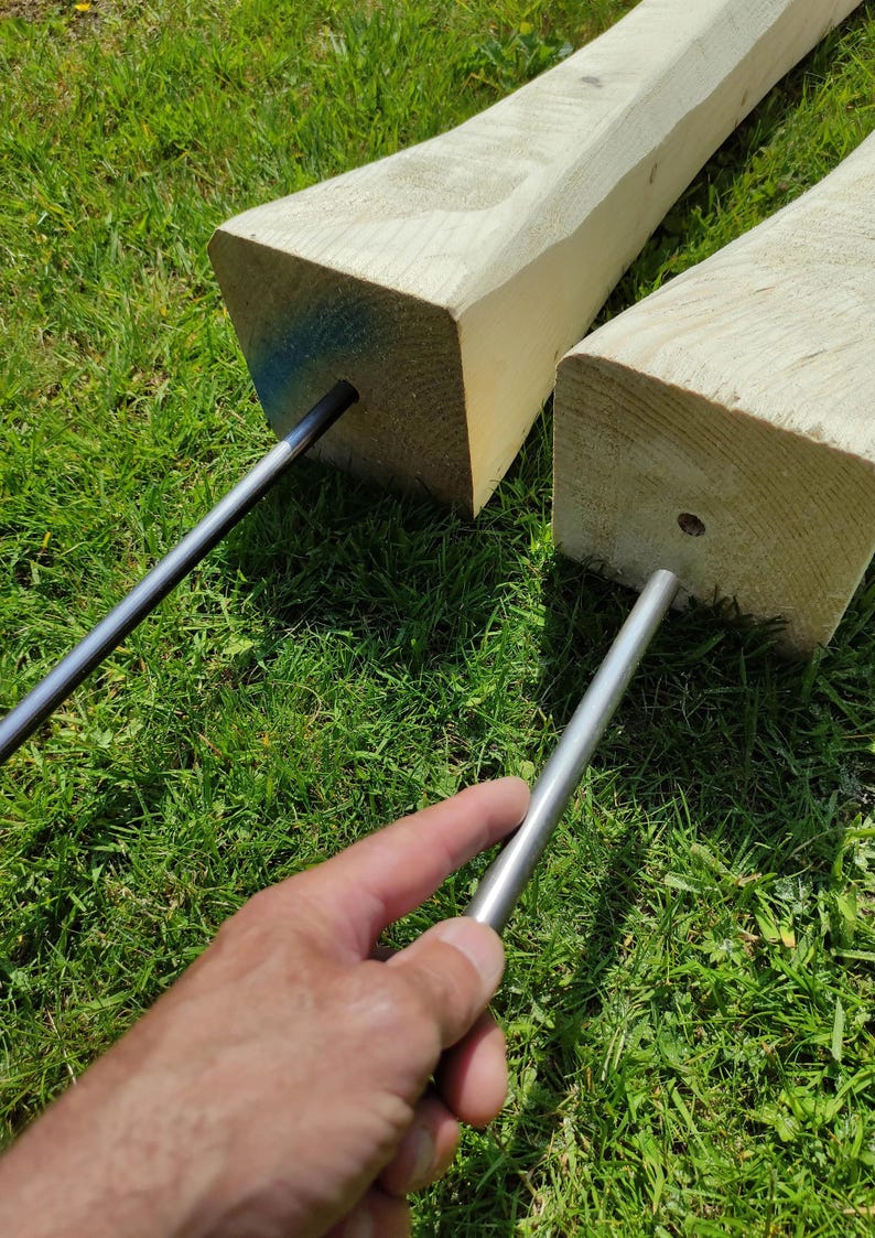 May include: Two wooden posts with metal rods inserted through holes in the top. The posts are on a bed of green grass.