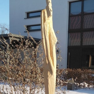 May include: A wooden sculpture of a person standing in front of a building with a large window. The sculpture is carved in a minimalist style and is made of light-colored wood.
