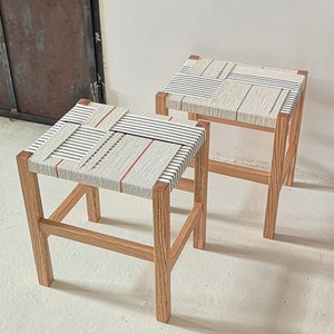 Peut inclure: Deux tabourets en bois avec des sièges en tissu tissé. Les sièges sont tissés avec des fils blancs, noirs et rouges. Les tabourets sont en bois naturel et ont un design simple et moderne.