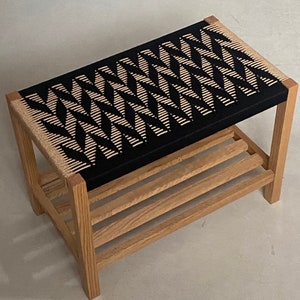 Puede incluir: Un banco de madera con un asiento tejido en blanco y negro y un estante debajo. El banco está hecho de madera natural y tiene un diseño simple y moderno.