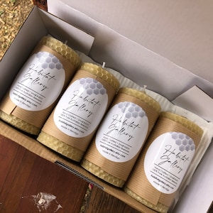 May include: Four natural beeswax candles in a box. The candles are wrapped in brown paper with a white label that says "Habitat Gallery" and includes the text "Hand Crafted Small Batch 100% Pure Australian Beeswax habitatgallery.etsy.com Made in Bendigo".