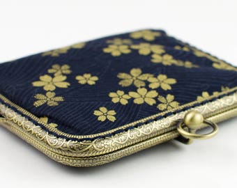May include: A small, navy blue coin purse with a gold floral pattern and a gold metal clasp. The purse has a decorative, ornate metal frame.