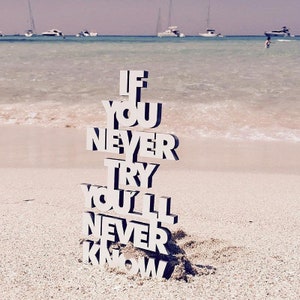 Peut inclure: Lettres en bois blanc épellant la phrase "If you never try you'll never know" sur une plage de sable avec une étendue d'eau en arrière-plan.