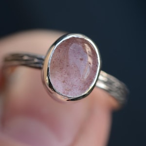 Könnte beinhalten: Ein silberner Ring mit einem hellrosa ovalen Edelstein.