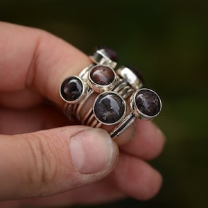 Könnte beinhalten: Ein Satz Silberringe mit dunkelbraunen und schwarzen Edelsteineinlagen. Die Ringe sind übereinander gestapelt.