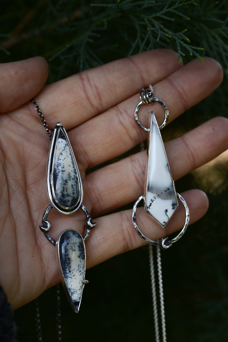 May include: Two silver necklaces with unique pendants featuring white and black agate stones. The pendants are both teardrop shaped and have intricate silver designs.
