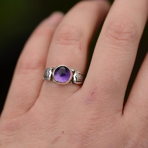 May include: A silver ring with a purple amethyst gemstone set in a textured band.