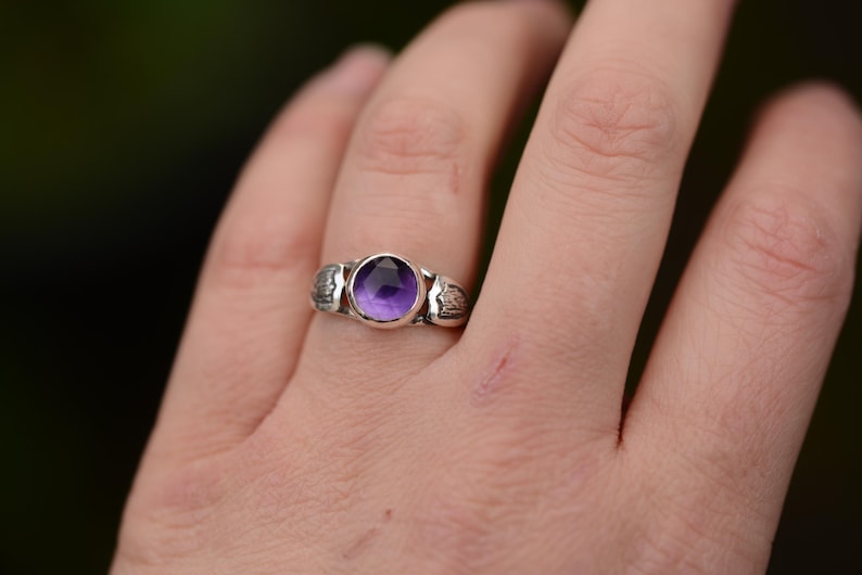 May include: A silver ring with a purple amethyst gemstone set in a textured band.
