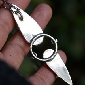 May include: A silver pendant necklace with a unique design featuring a circle with a smaller circle inside. The pendant is attached to a silver chain.